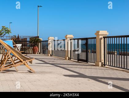 Eine Terrasse mit zwei Liegestühlen mit Blick auf das blaue Meer an einem sonnigen und klaren Sommernachmittag Stockfoto