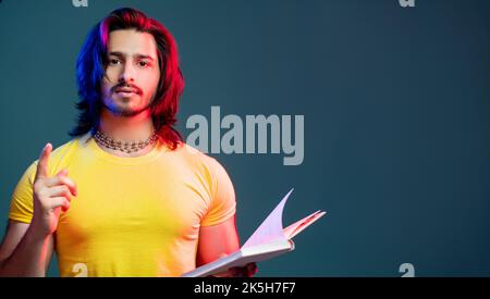 Intelligenter Hipster-Mann. Eureka-Geste. Neonlicht im Porträt. Finden Sie eine Entscheidung. Nachdenklicher bärtiger Hipster, der den Buchfinger in blau-roter Neonfarbe hochhält Stockfoto
