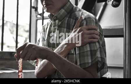 Schmerzen im Oberarm des älteren Mannes aus Südostasien. Konzept der gefrorenen Schulter. Stockfoto