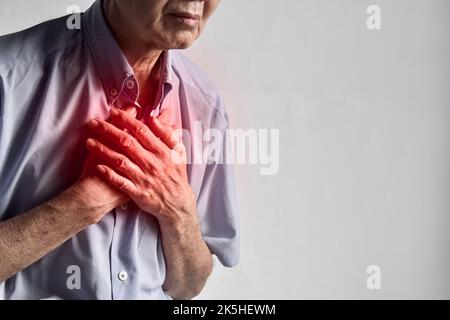Älterer Mann aus Asien, der an zentralen Brustschmerzen leidet. Brustschmerzen können durch Herzinfarkt, Myokardinfarkt oder Ischämie, Myokarditis, Lungenentzündung, o verursacht werden Stockfoto