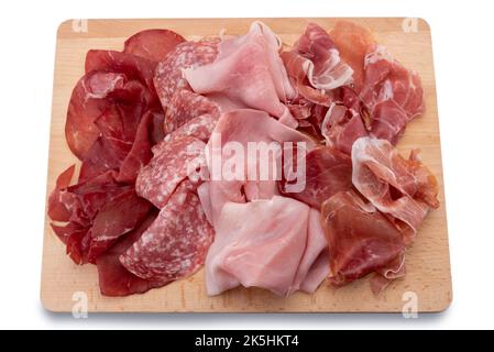 Aufschnitt auf Holzschneidebrett, Scheiben aus Brosaola, Salami, Schinken und Parmaschinken, isoliert auf Weiß Stockfoto