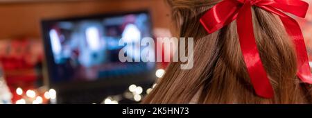 Hinter dem weiblichen Kopf lange blondie Haare und roten Bogen Rückansicht beobachten den weihnachtsfilm auf Laptop auf Camping Home in gemütlichen Bett mit leuchtenden Lichtern garl Stockfoto