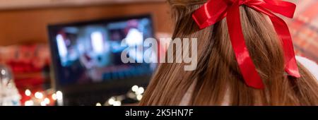 Hinter dem weiblichen Kopf lange blondie Haare und roten Bogen Rückansicht beobachten den weihnachtsfilm auf Laptop auf Camping Home in gemütlichen Bett mit leuchtenden Lichtern garl Stockfoto
