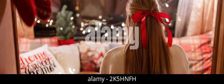 Gesichtslose Frau mit langen blondie Haaren und roten Bogen Haarclip Genuss entspannen zu Hause in gemütlichen bequemen Bett mit leuchtenden Lichtern Girlande Bokeh in der Nacht auf ch Stockfoto