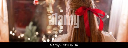 Gesichtslose Frau mit langen blondie Haaren und roten Bogen Haarclip Genuss entspannen zu Hause in gemütlichen bequemen Bett mit leuchtenden Lichtern Girlande Bokeh in der Nacht auf ch Stockfoto