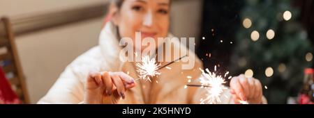 Verschwommene junge ehrliche Frau, die in den Händen hält, glänzt mit einem roten karierten Feuer im Freien an einem glücklichen Neujahr und fröhlichen weihnachtsfeiertagen Stockfoto