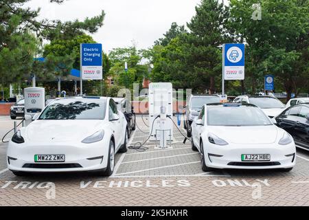 POOLE, Großbritannien - 07. Juli 2022. Zwei weiße Tesla-Elektroautos tanken an einer Ladestation für Elektroautos auf einem Tesco-Parkplatz Stockfoto