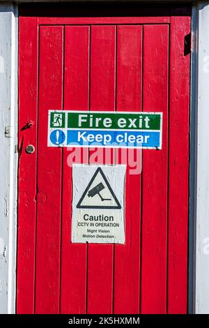 Dorking Surrey Hills Großbritannien, 08 2022. Oktober, Feuerausgang und klares Schild an Einer rot lackierten Holztür ohne Personen halten Stockfoto