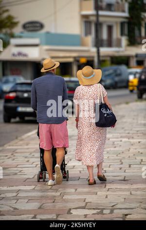 Ein junges Paar, das mit dem Kinderwagen läuft, ein Paar mit Baby, ein Paar im Urlaub mit Baby, ein Paar im Urlaub mit einem Kind, ein junges Paar mit Sonnenhut. Stockfoto