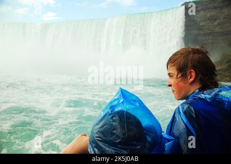 Die Kinder der Maid of the Mist Bootstour in den Niagarafällen werden durchnässt, während sie sich in der Nähe der kanadischen Horseshoe Falls befinden, obwohl sie ihre blauen Ponchos beschwingten Stockfoto