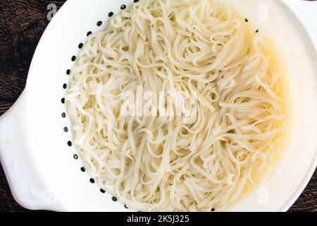 Gekochte und abgetropfte Reisnudeln in einem weißen Kunststoffsieb: Nahaufnahme von oben von gekochten Nudeln in einem Sieb Stockfoto