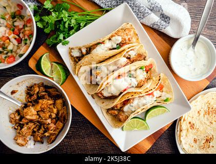 Chicken Tacos gekrönt mit Pico de Gallo und Cilantro-Limette Sauce: Gegrillte Chicken Tacos umgeben von Belägen und Tortillas Stockfoto