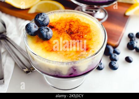 Heidelbeere-Orange Creme Brulee garniert mit frischen Heidelbeeren: Orangen-Vanille-Pudding über Heidelbeermarmelade mit karamellisiertem Zucker Stockfoto