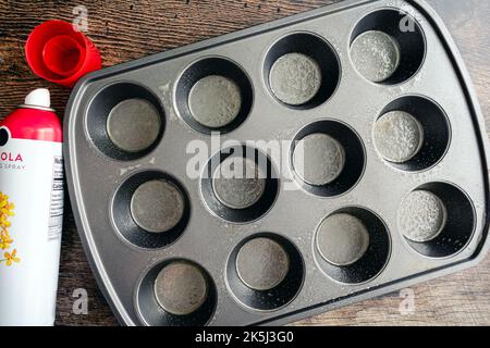 Antihaftbeschichtete Metallmuffinform, mit Rapsöl versprüht: Gefettete antihaftbeschichtete Muffin-Pfanne mit einer Aerosolflasche mit Kochspray Stockfoto