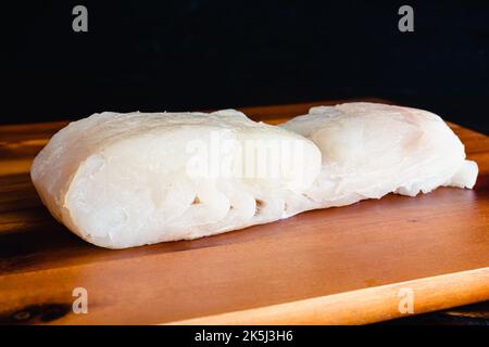 Nahaufnahme Seitenansicht eines rohen, frischen Halibut-Filets: Ungekochte, frische weiße Fischfilets auf einem Holzschneidebrett Stockfoto