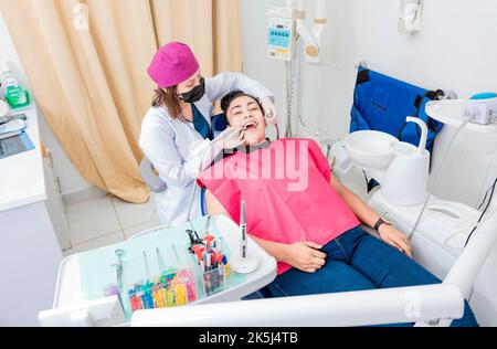 Stomatologin Frau, die die Zähne eines Patienten reinigt, hoher Winkel des Stomatologen, der die Zähne einer Frau reinigt, Zahnärztin, die den Mund eines Patienten mit einem reinigt Stockfoto