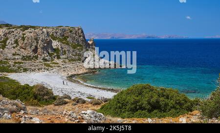 Agios Pavlos Strand, Kiesstrand, karge Felsen, Bäume, blaues Meer, Grünes Meer, Halbinsel Gramvoussa, zwei Wanderer am Strand, fast wolkenlos blau Stockfoto