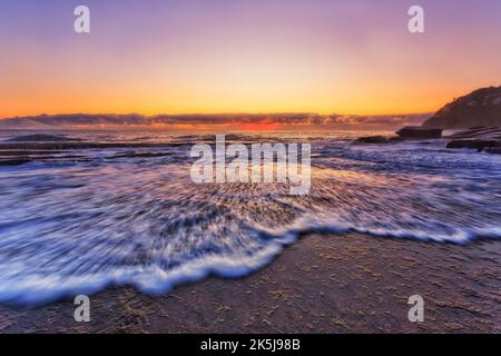 Szenische bunte einlaufende Welle auf Walstrand Sandsteinfelsen bei Sonnenaufgang - Pazifik Seeseppe. Stockfoto