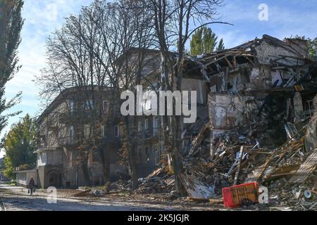 Slowiansk, Donezk, Ukraine. 8. Oktober 2022. Eine Frau kommt an einem Wohngebäude vorbei, das von einem russischen Beschuss in Slowiansk zerstört wurde. In den letzten Wochen hat die ukrainische Armee in einer erfolgreichen Gegenoffensive große Teile des Territoriums zurückerobert, die russische Truppen gezwungen hat, lange gehaltene Positionen aufzugeben. In dem, was Kiew als Moskaus Reaktion auf seine Niederlagen beschreibt, hat Präsident Wladimir Putin vier teilweise besetzte Regionen der Ukraine eingegliedert. Die Annexionen, die weithin als illegal abgetan wurden, haben Befürchtungen über eine mögliche Eskalation im siebenmonatigen Krieg geweckt. (Bild: © Andriy Andriyen Stockfoto