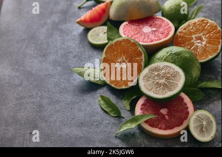 Von oben aus verschiedene halbierte Zitrusfrüchte mit Limette und Grapefruit auf grauem Hintergrund mit Blättern in hellem Raum platziert Stockfoto