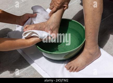 Die weibliche Pflegekraft wischt die Füße der älteren Frau mit einem Handtuch ab. Stockfoto