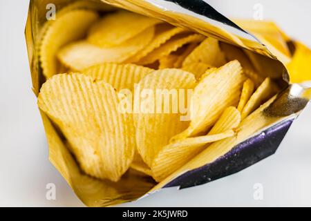 Ansicht von trockenen knusprigen frittierten Wellkartoffelchips in offener Tüte auf weißem Hintergrund, selektiver Fokus. Stockfoto