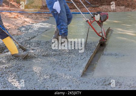 Mithilfe einer Stampfmaschine wird verdichteter Frischbeton auf die neue Auffahrtkonstruktion ausgerichtet. Stockfoto