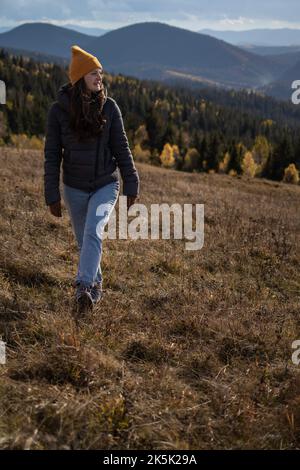 Junge glückliche Frau in orangefarbener Mütze läuft vor der Berglandschaft Stockfoto