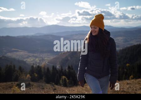 Junge glückliche Frau in orangefarbener Mütze läuft vor der Berglandschaft Stockfoto