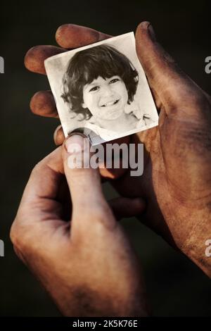 Umgang mit Verlusten. Eine mit Ruß bedeckte Hand, die ein schwarz-weißes Bild eines kleinen Jungen hält. Stockfoto