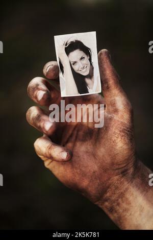 Dieses Bild hält mich in Gang. Eine mit Ruß bedeckte Hand, die ein schwarz-weißes Bild einer schönen Frau hält. Stockfoto