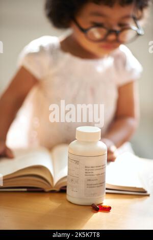 Medikamente haben viele Verwendungen. Ein kleines Mädchen zu Hause allein mit Pillen auf dem Tisch vor ihr. Stockfoto