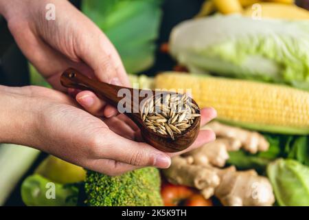 Ganze Haferflocken in einem Holzlöffel, Nahaufnahme auf einem Hintergrund von Gemüse. Stockfoto