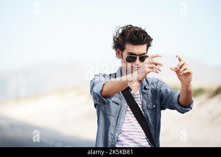 Ich habe einige Erinnerungen an meine Reise bewahrt. Trendiger junger Mann, der auf der Straße steht und ein Foto auf seinem Handy fotografiert. Stockfoto