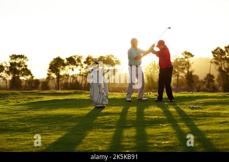 Hier möchten Sie Ihren Schwung starten. Ein Golfer, der auf dem Golfplatz Hilfe von seinem Caddy erhält. Stockfoto