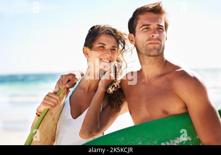 Eine Leidenschaft für das Surfen teilen. Junges Paar schaut sich an, bevor es zum Surfen geht - Copyspace. Stockfoto