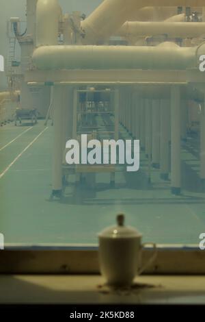 Blick auf eine weiße Teetasse mit Deckel in der Nähe des Fensters eines LNG-Schiffes auf See Stockfoto