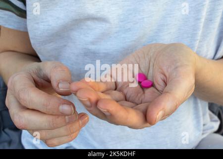 Person Hand mit Pillen. Frau hält zwei rosa Pillen in der Hand. Gesundheitswesen, Medizin Konzept. Der Patient nimmt Medikamente, Nahrungsergänzungsmittel, Antibiotika Stockfoto