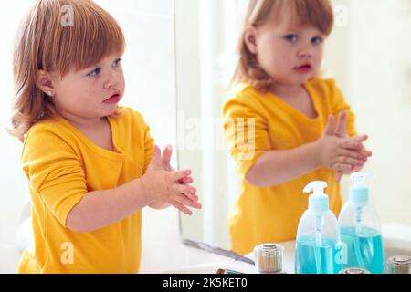 Ein kleines Mädchen, das in den Spiegel schaut, während sie ihre Hände wäscht. Stockfoto