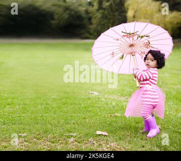 Es ist im Begriff, echte Phantasie hier oben zu bekommen. Ein entzückendes kleines Mädchen spielt mit einem rosa Regenschirm draußen. Stockfoto