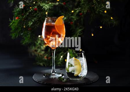 Cocktail namens Orangenspritz und Gin Tonic oder Moscow Mule in dunkler Partylaune. Feier-Szene mit dunklem Hintergrund. Weihnachts- oder Neujahrsparty dez Stockfoto