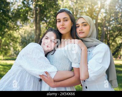 Eine Gruppe von Frauen umarmt, zeigt Vielfalt, Unterstützung und Solidarität gemeinsam, gegen Wald- oder Gartenhintergrund. Multikulturelle Freunde stehen in Einheit, in Stockfoto