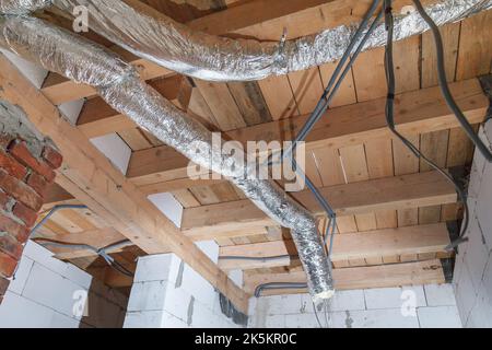 Installation einer Rohrheizung. Heizen zu Hause mit heißer Luft. Verlegung und Befestigung isolierter Rohre an der Decke. Stockfoto