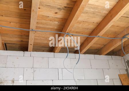 Elektrische Leitungen an einer Holzdecke überlappen. Elektriker in einem Wohngebäude. Elektrische Leitungen während des Baus des Hauses Stockfoto