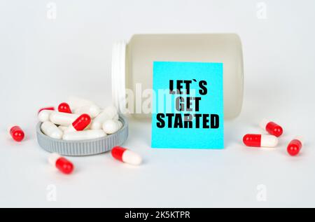 Medizinisches Konzept. Auf grauem Hintergrund ein Glas, Kapseln und ein Schild mit der Aufschrift - los geht's Stockfoto