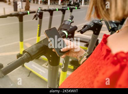 Die Hand einer Frau scannt mit einem Mobiltelefon den QR-Code eines Rollers Stockfoto