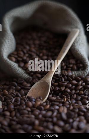 Kaffeebohnen im Jutebeutel und Holzlöffel auf dem Tisch Stockfoto