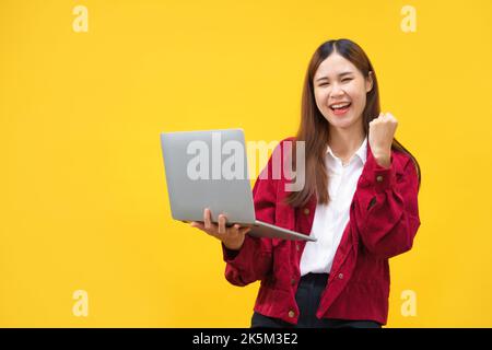 Frauen halten Laptop und heben den Arm, um mit leerem Platz auf isoliertem gelben Hintergrund zu feiern. Stockfoto