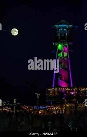 Brighton, East Sussex, England. 08. Oktober 2022. Ein (97,5%) Vollmond erhebt sich über dem Strand in Brighton und wird hier hinter dem Reißleine vom Brighton Pier aus gesehen glühend gesehen.©Sarah Mott / Alamy Live News. Stockfoto