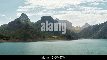Panoramablick auf den gipfel des gilbo und seine nahen Berge am stausee Riaño gelegen, erhellen türkisfarbene Gewässer unter dem blauen Himmel die Gipfel Stockfoto